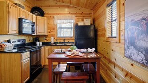 Uma cozinha estilo cabana, com paredes de madeira, uma geladeira preta, micro-ondas e uma mesa de jantar posta com pratos e um vaso de flores.
