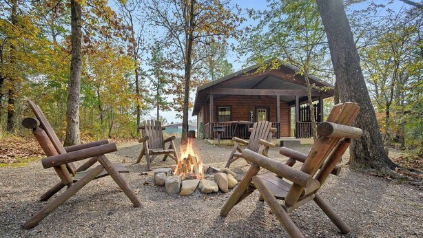 Uma cabana com lareira e cadeiras Adirondack em meio a uma floresta.