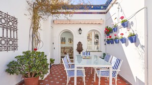 Un patio con una mesa de vidrio, sillas a rayas, una planta en maceta y macetas colgantes de flores.
