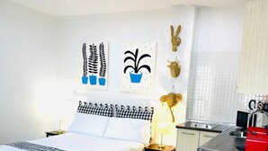 Habitación de hotel con cama, mesita de noche, lámpara y una pequeña kitchenette.