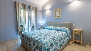 A bedroom with a bed, curtains, a bedside lamp, a nightstand, and a wall-mounted light fixture. - Vacation Home "Ibiscus Rosa 1" with Mountain View, Terrace & A/C (Geremeas)