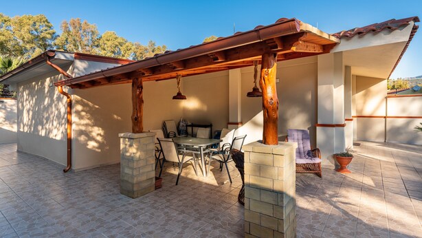 A covered patio area with a table and chairs, a hanging light fixture, and a view of the surrounding landscape. - Vacation Home "Ibiscus Rosa 1" with Mountain View, Terrace & A/C (Geremeas)