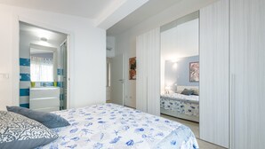 Quarto com cama, mesa de cabeceira, guarda-roupa e banheiro visível por uma porta aberta.
