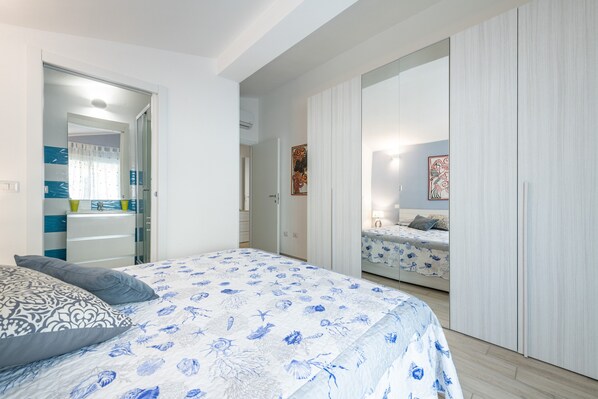 Een slaapkamer met een bed, nachtkastje, kast en een badkamer zichtbaar door een geopende deur.