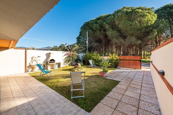 A patio with a grill, chairs, and a small garden area.