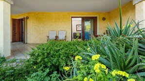 A covered outdoor area with a yellow wall, two white chairs, and a door leading inside.