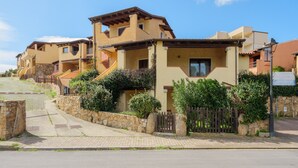 A residential building with multiple balconies, stone walls, and a paved entrance.