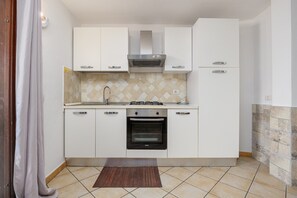 Una cocina compacta con armarios blancos, estufa a gas, horno y salpicadero de azulejos.