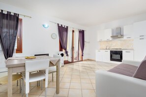 Eine moderne Küche mit weißen Schränken, einem Herd und einer Mikrowelle. Es gibt einen Essbereich mit Tisch und Stühlen, sowie ein Sofa im Wohnbereich.