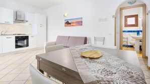 Una cocina moderna con armarios blancos, una mesa de comedor con un mantel decorativo y un cuadro de un atardecer en la pared.