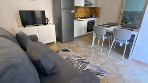 Una sala moderna con un sofá, televisor y una cocina con refrigerador, estufa y mesa de comedor.