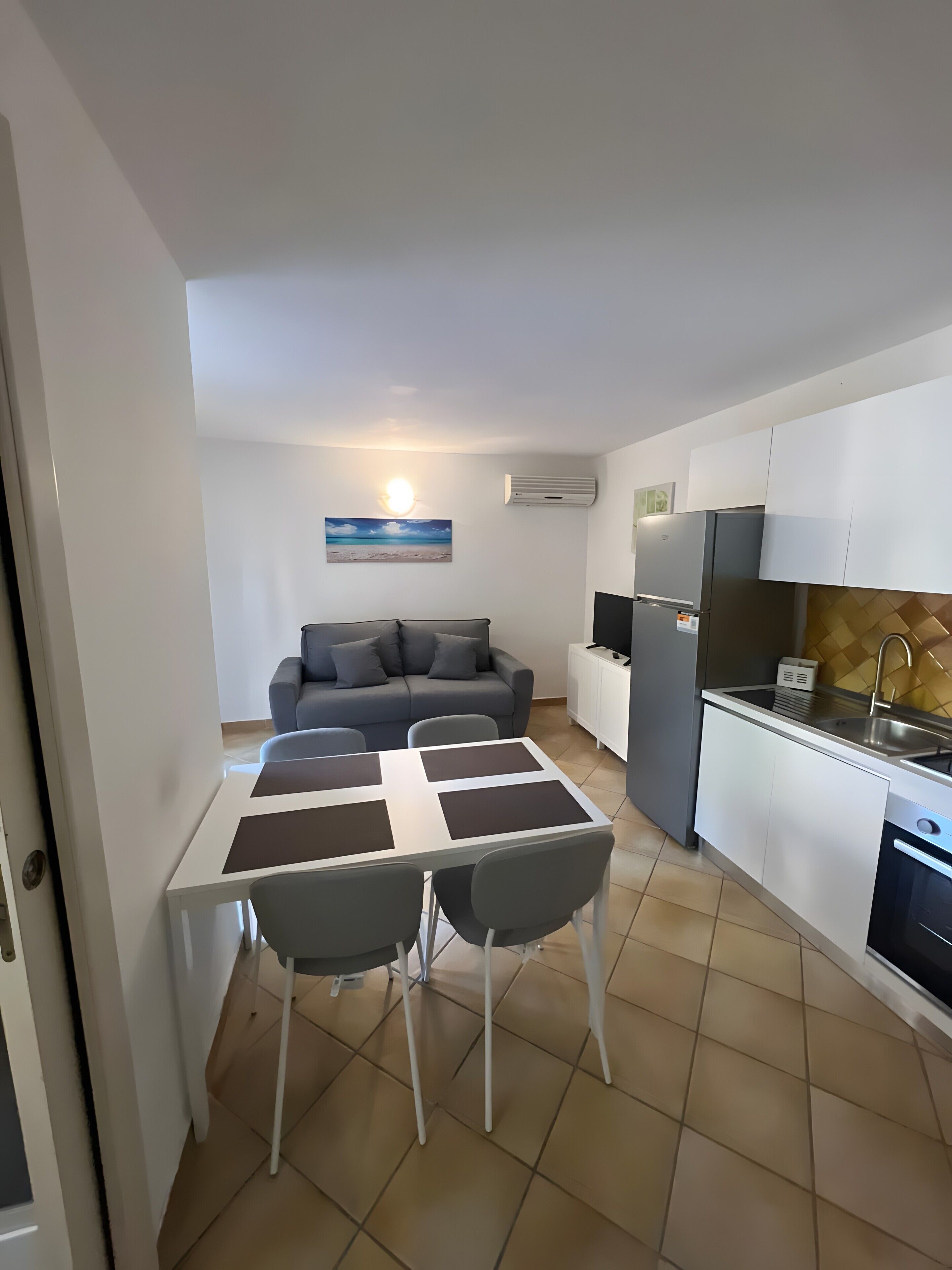 Un espacio habitable compacto con kitchenette, un comedor con mesa y sillas, un sofá y aire acondicionado instalado en la pared.