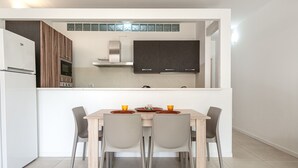 A modern kitchen with dark cabinets, a white refrigerator, and a dining area with a wooden table and four chairs.