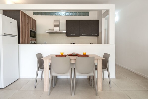 Una cocina moderna con armarios oscuros, un refrigerador blanco y un comedor con una mesa de madera y cuatro sillas.