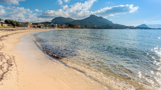 A beach with clear water, a sandy shore, and distant mountains.