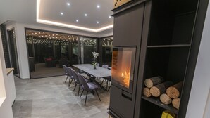 Ein modernes Wohnzimmer mit Kamin, Esstisch mit Stühlen und einem großen Fenster mit Lichterkette.