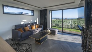 Ein modernes Wohnzimmer mit einem grauen Sofa, einem Couchtisch und Blick auf ein Weinberg durch große Fenster.