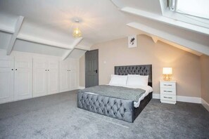 A bedroom with a tufted headboard bed, a bedside lamp, and a white wardrobe.