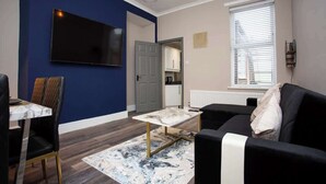 A living room with a TV, sofa, dining table, and chairs. - Modern Interior Spacious  Four Bedroom Apartment (South Shields)