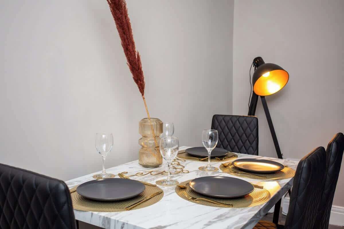 A dining table set with black plates, gold placemats, and clear wine glasses.