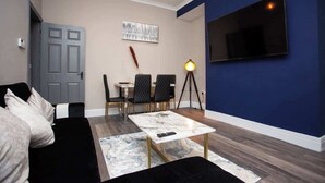 A living room with a sofa, a coffee table, a TV, a dining area with chairs, and a lamp. - Modern Interior Spacious  Four Bedroom Apartment (South Shields)