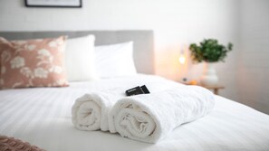 A neatly made bed with rolled white towels and a black object on top. - 8 on Clarence - perfectly located in the centre of town (Moss Vale)