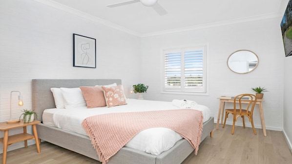A modern bedroom with a bed, bedside table, chair, and a window with blinds.