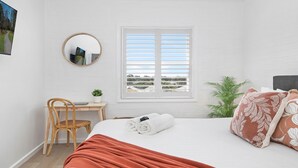 Quarto com cama, escrivaninha, cadeira, janela com persianas e espelho na parede.