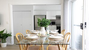 A dining area with a glass table, wicker chairs, and a white vase with a plant.