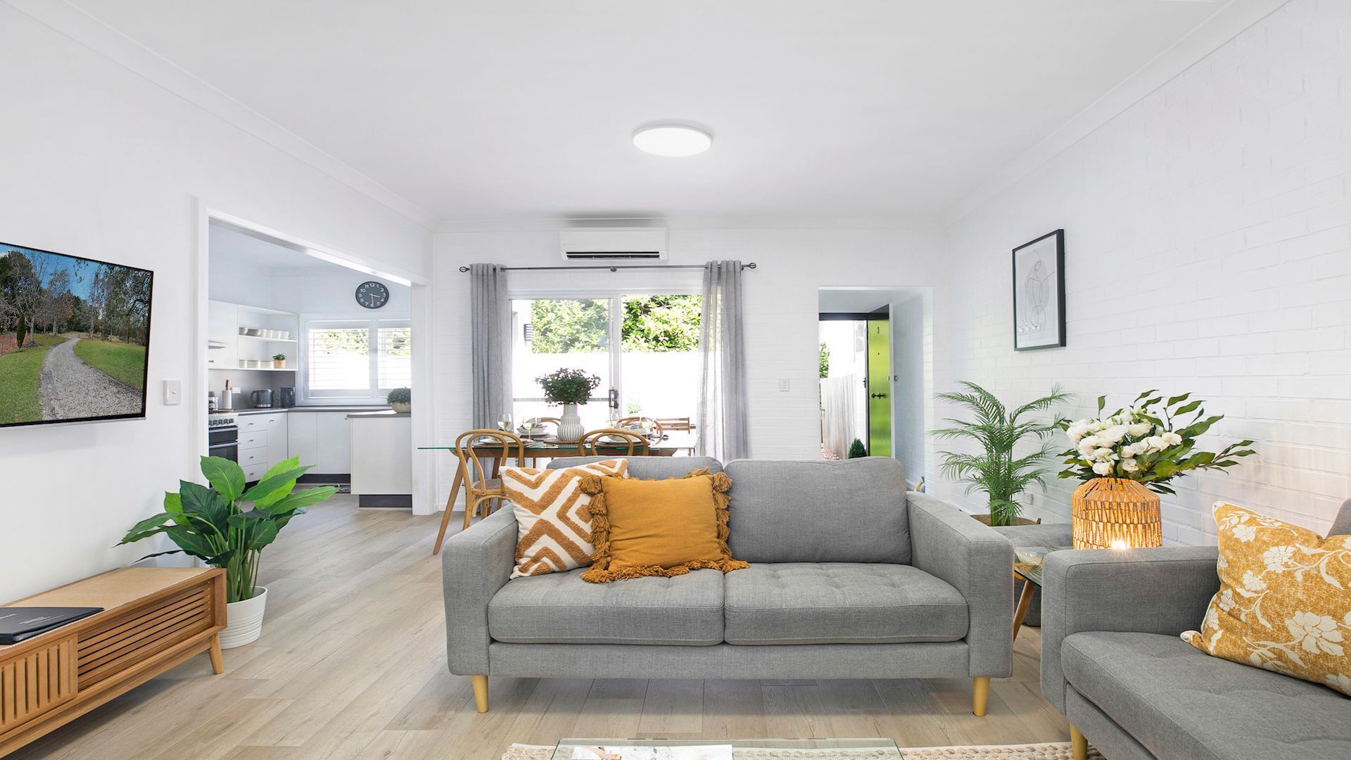 Ein modernes Wohnzimmer mit einem grauen Sofa, einem Holztisch und einem Essbereich mit Tisch und Stühlen.