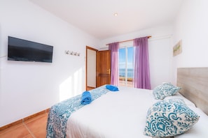 A bedroom with a bed, a TV mounted on the wall, a door, and a window with curtains.