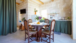 A dining area with a round table, chairs, a TV mounted on the wall, and a kitchen in the background.