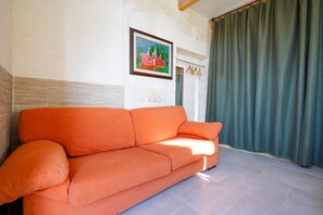A room with a sofa, a painting on the wall, and a curtain.