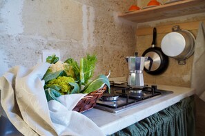 A kitchen with a gas stove, a basket of fresh vegetables, and a hanging pan.