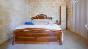 A bedroom with a wooden bed, a nightstand, a wardrobe, and a stone wall.