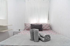 Ein ordentlich eingerichtetes Schlafzimmer mit Bett, Kissen, Nachttisch und einem Fenster mit Vorhängen.