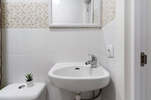Une salle de bain avec un lavabo blanc, une petite plante en pot et des toilettes.