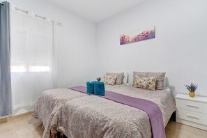 A bedroom with a bed, pillows, a nightstand, a potted plant, and a window with curtains.