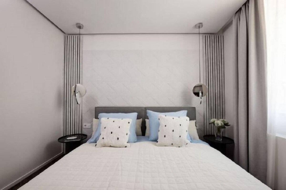 A modern hotel room with a large bed, two bedside tables, and a nightstand.