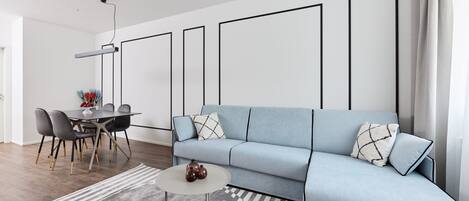 A modern living room with a light blue sofa, a round coffee table, and a dining area with a table and chairs.