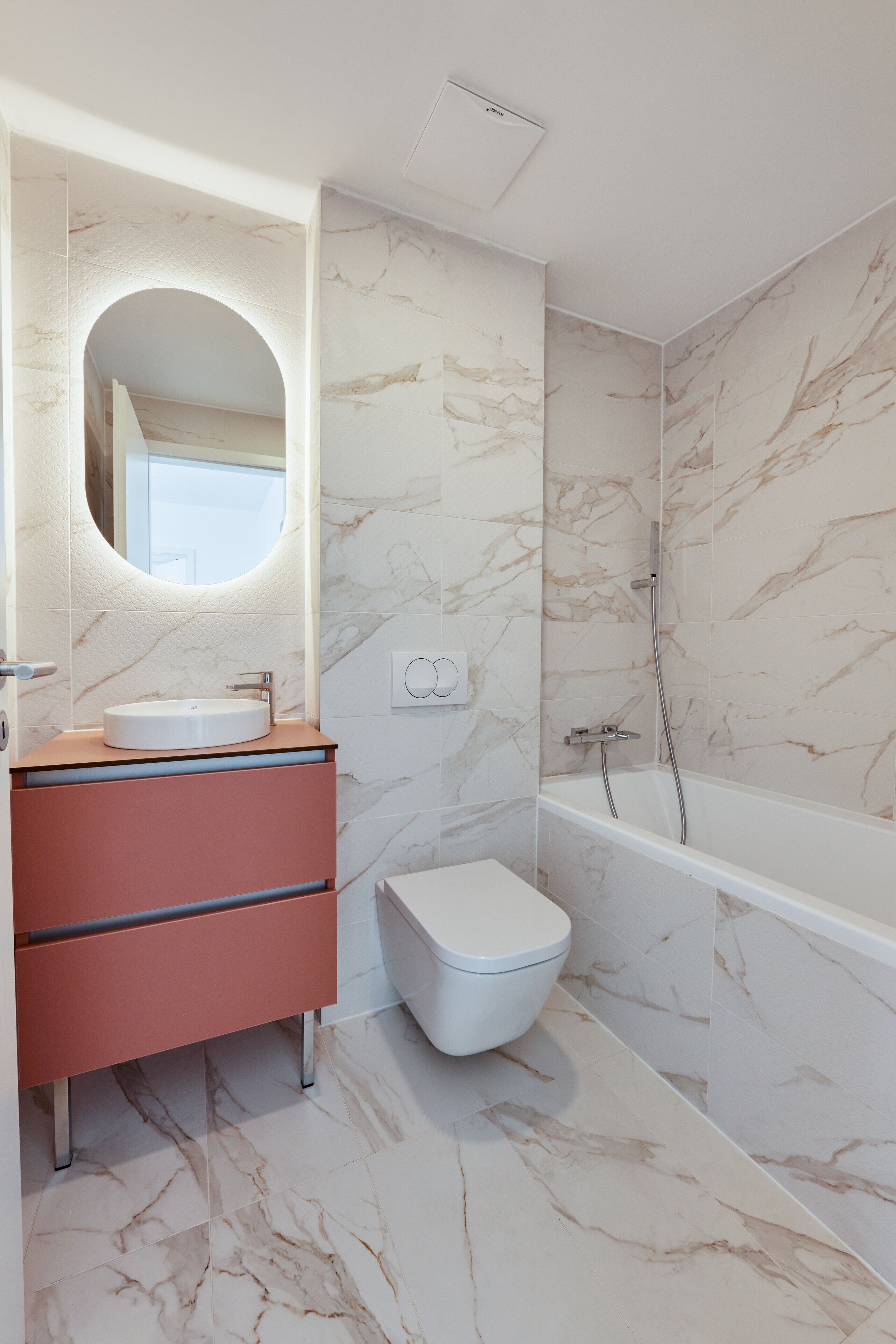 Ein Badezimmer mit Marmorwand, Waschbecken in Weiß, Spiegel, Toilette und Badewanne.