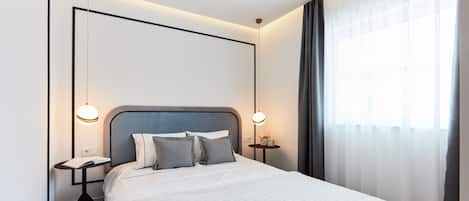 A modern hotel room with a large bed, bedside tables, and a window with curtains.