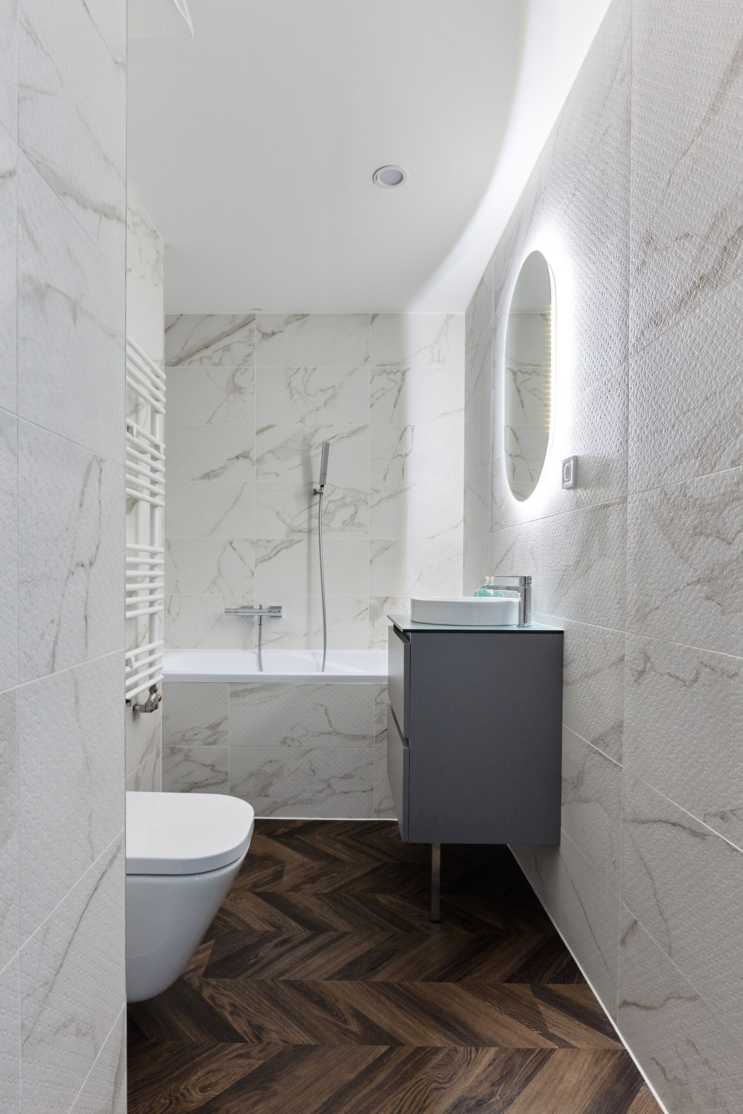 A modern bathroom with a marble wall, a wooden floor, a toilet, a sink, and a shower.
