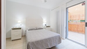 Un dormitorio con cama, mesitas de noche, ventilador de techo y puerta corrediza de vidrio a un balcón.