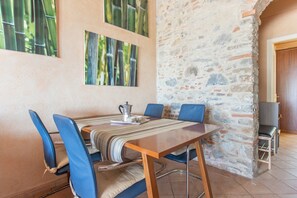 A dining area with a stone wall, a wooden table, blue chairs, and a television.