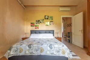 A bedroom with a bed, a nightstand, a wall-mounted air conditioner, and a door leading to another room.