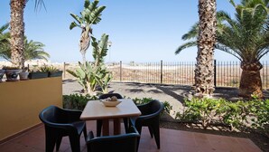 Eine Terrasse mit Tisch und Stühlen, umgeben von Palmen und Blick auf eine Wüstenlandschaft.