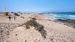 Ein Strand mit einem Rettungsturm, felsigem Gelände und Menschen, die am Ufer entlanggehen.