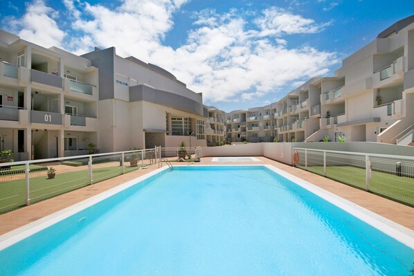 Un edificio moderno con piscina, balcones y cielo despejado.