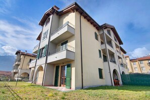Un immeuble résidentiel à plusieurs étages, doté de balcons, d’une entrée principale et entouré d’une zone verdoyante.